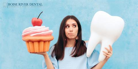 Woman holding a cupcake in one hand and a fake tooth in the other looking confused on which to choose