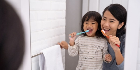 mother and daughter brushing teeth and looking in the mirror
