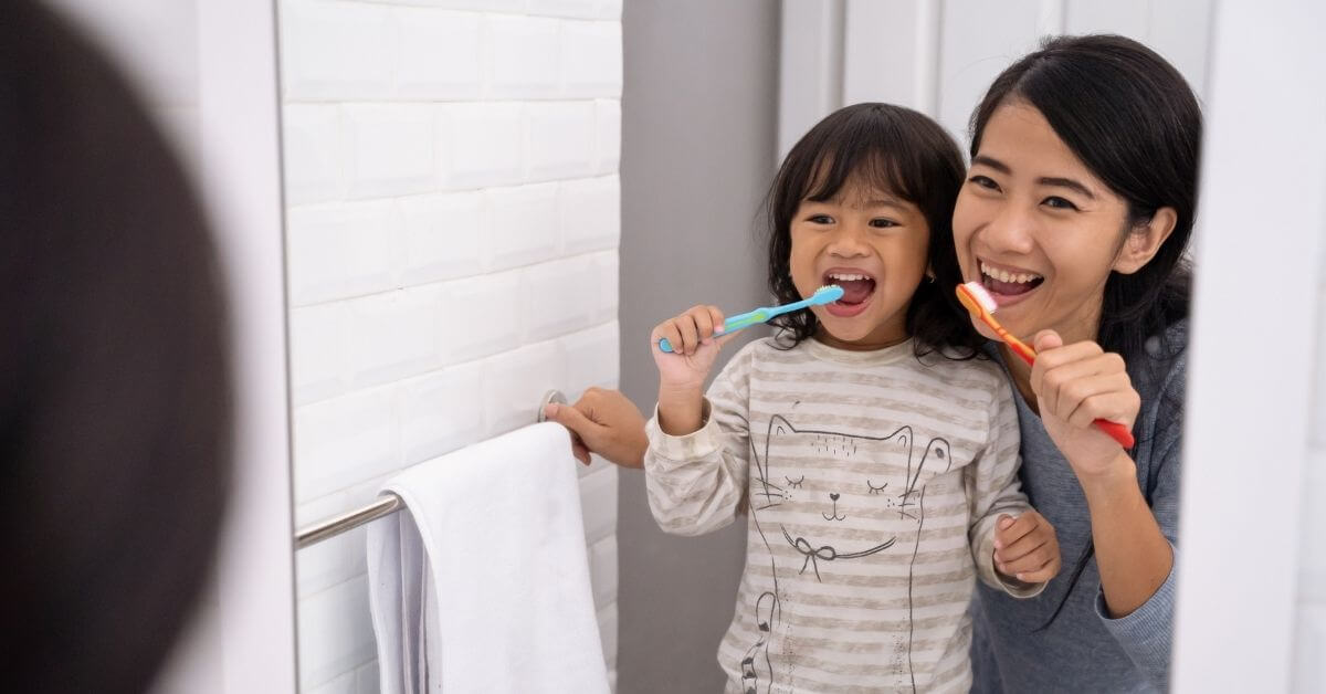 mother and daughter brushing teeth and looking in the mirror